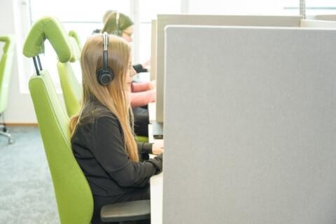 Istekkiläinen istumassa työpisteellä koneella ja hänellä on kuulokkeet päässään.